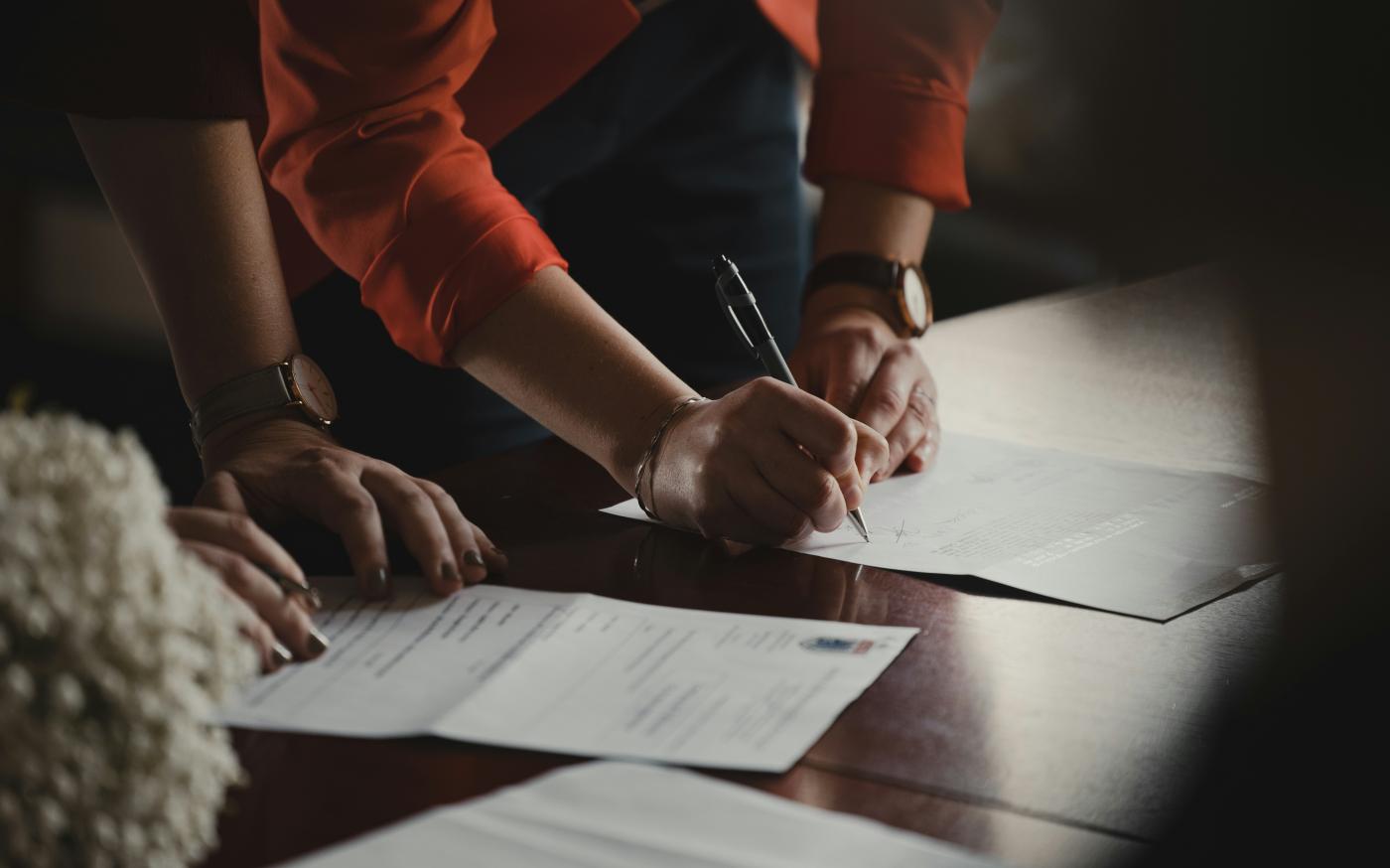 person in orange long sleeve shirt writing on white paper by Romain Dancre courtesy of Unsplash.