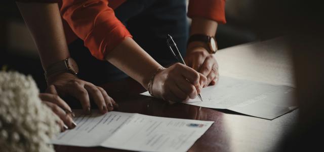 person in orange long sleeve shirt writing on white paper by Romain Dancre courtesy of Unsplash.